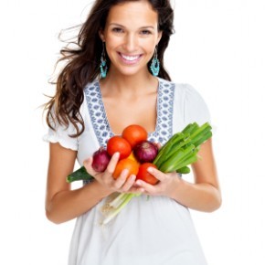 Женщина вегетарианец с руками, полными овощей.